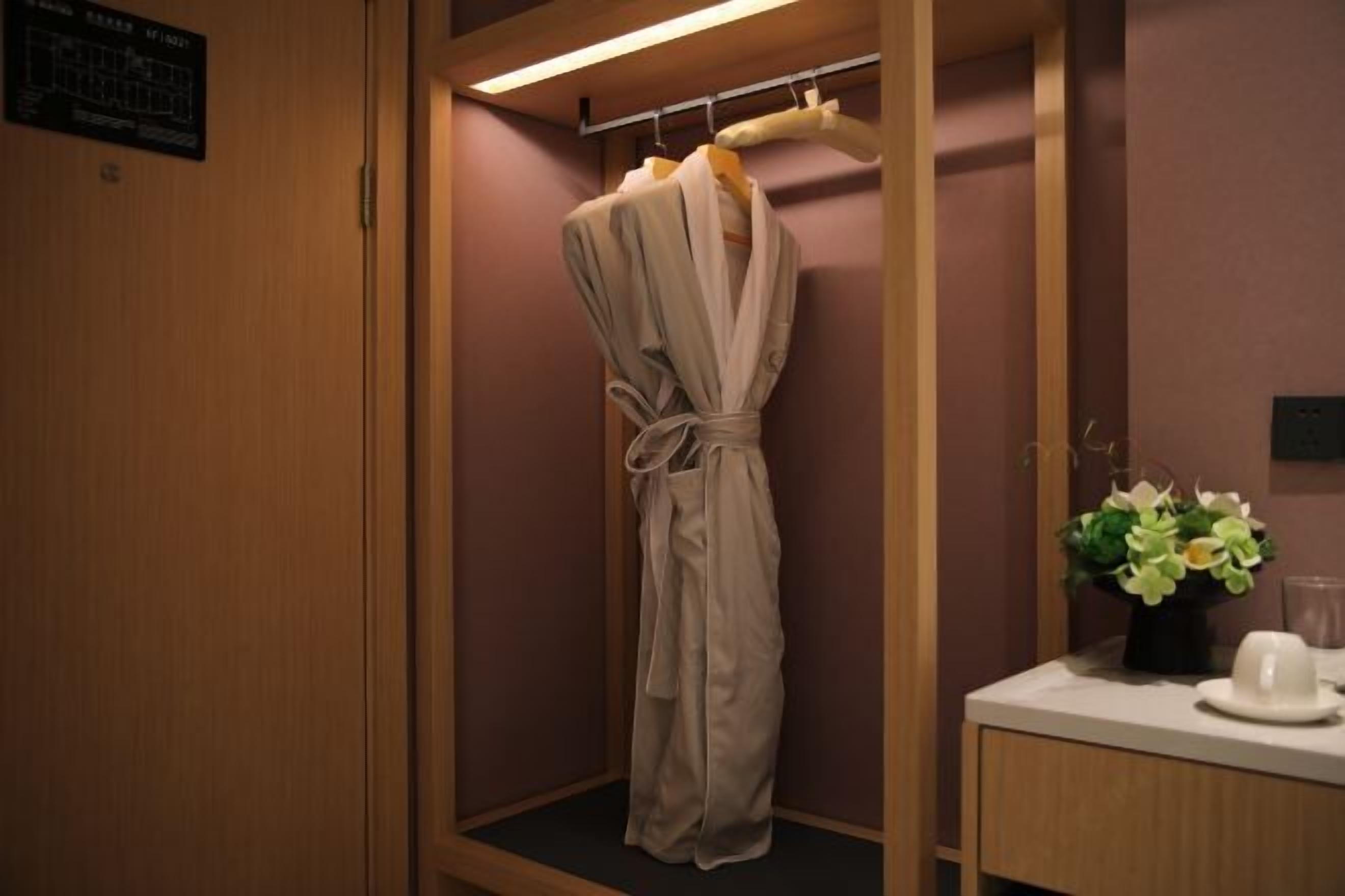A wooden-framed walk-in closet with a robe hanging on a rack, a small table with a vase of flowers, and a wall-mounted sign.