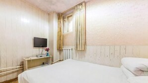 A bedroom with a bed, a TV on a stand, a radiator, and a window with curtains. - Shun Feng Yuan Hostel (Qingdao)