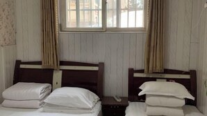 A room with two beds, each with white bedding and wooden headboards. There is a window with curtains, and a small table between the beds. - Shun Feng Yuan Hostel (Qingdao)