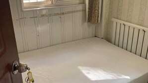 A room with a white bed, a window with a curtain, and a radiator. - Shun Feng Yuan Hostel (Qingdao)