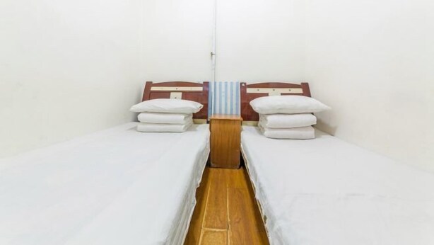 A small, clean room with two single beds, a wooden nightstand, and a striped towel hanging between the beds. - Shun Feng Yuan Hostel (Qingdao)