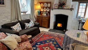 A cozy living room with a fireplace, a sofa set, a patterned rug, and a wooden cabinet with decorative items. - The Boathouse (Bucks Mills)