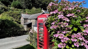 A traditional red telephone booth with a stone building in the background. - The Boathouse (Bucks Mills)