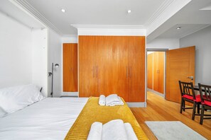 A hotel room with a bed, a yellow towel, a wooden wardrobe, a chair, and a desk. - Prestige studio flat

 (London)