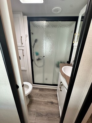 A compact bathroom with a toilet, a sink, and a shower with frosted glass doors. - Key Largo, Charming 2-bedroom RV in Calusa Campground (Key Largo)