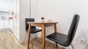 A small dining area with a wooden table and two black chairs, a white wall, and a kitchen area with white cabinets and a red appliance. - "Las Damas de Madrid 10 minutes from downtown" (Madrid)