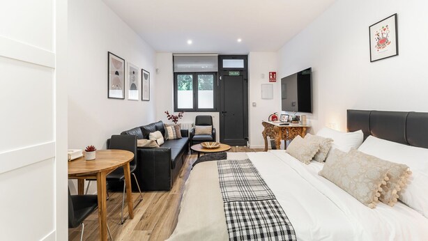 A modern hotel room with a large bed, a sofa, a dining table, and a TV. - "Las Damas de Madrid 10 minutes from downtown" (Madrid)