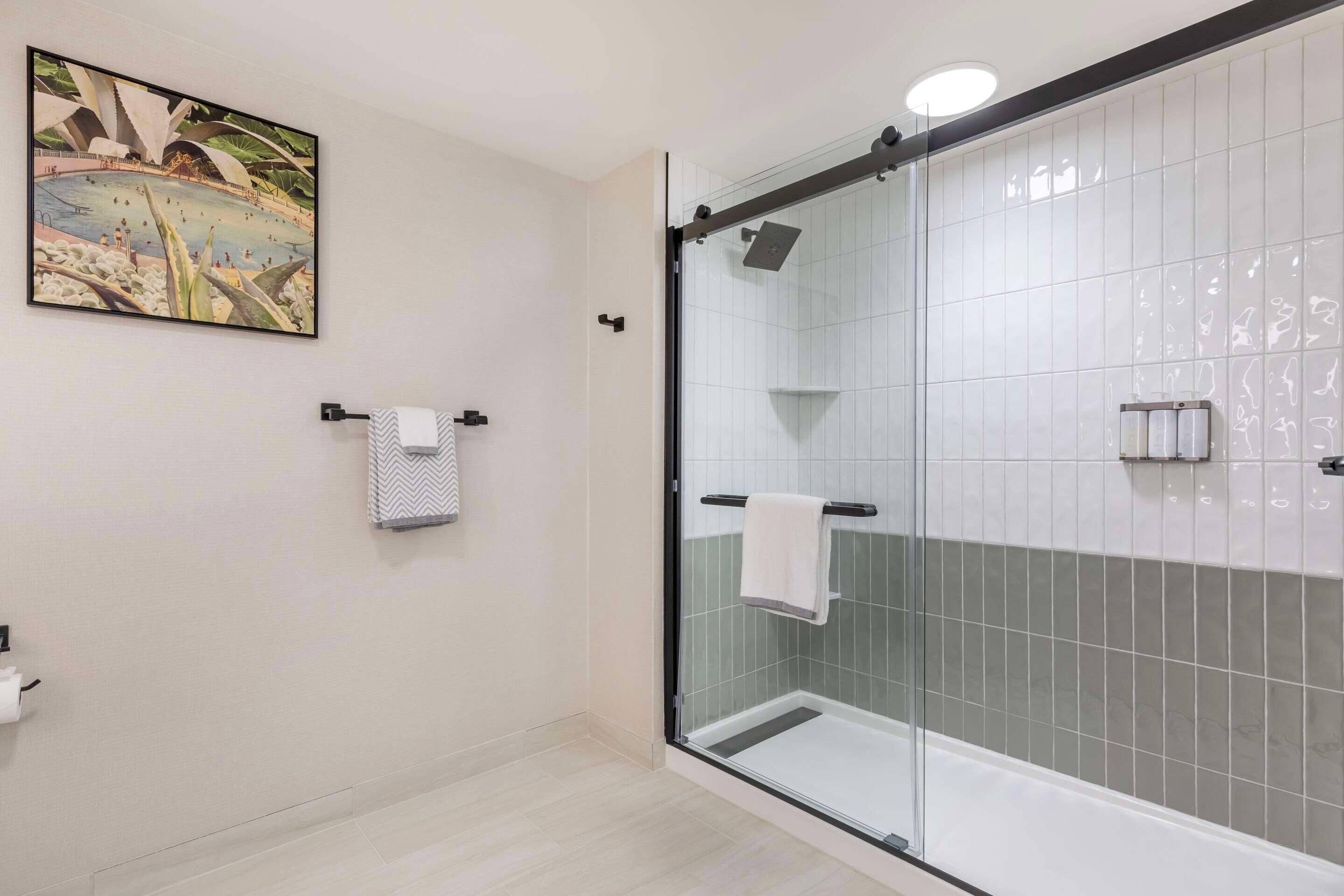 A modern bathroom with a glass-enclosed shower, white tiled walls, and a framed picture on the wall.