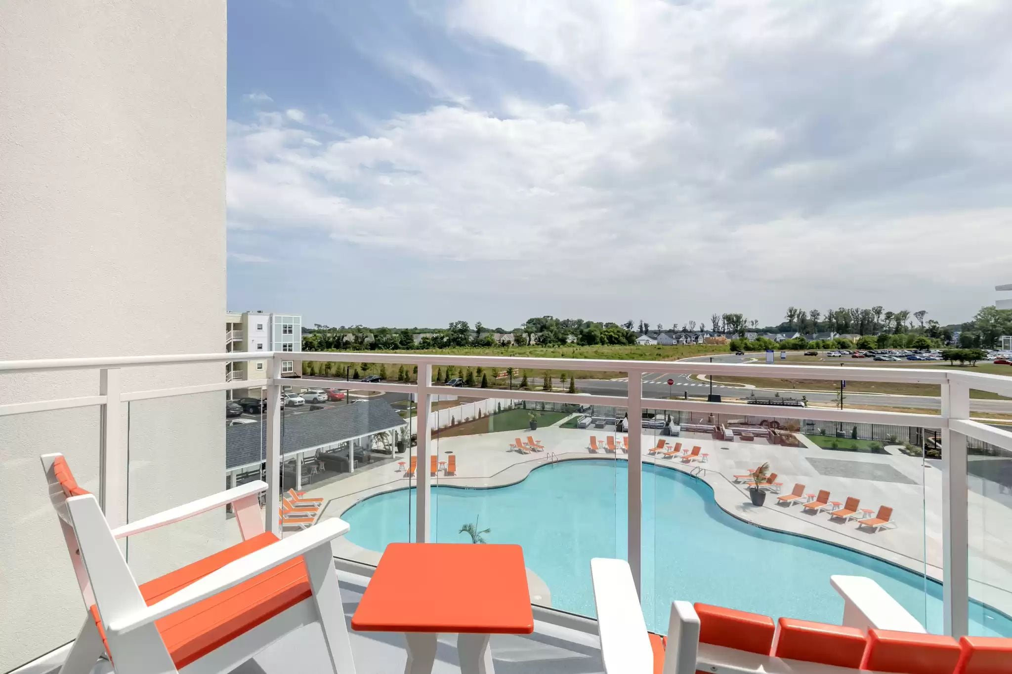 A balcony with a pool view, white and orange furniture, and a clear sky.