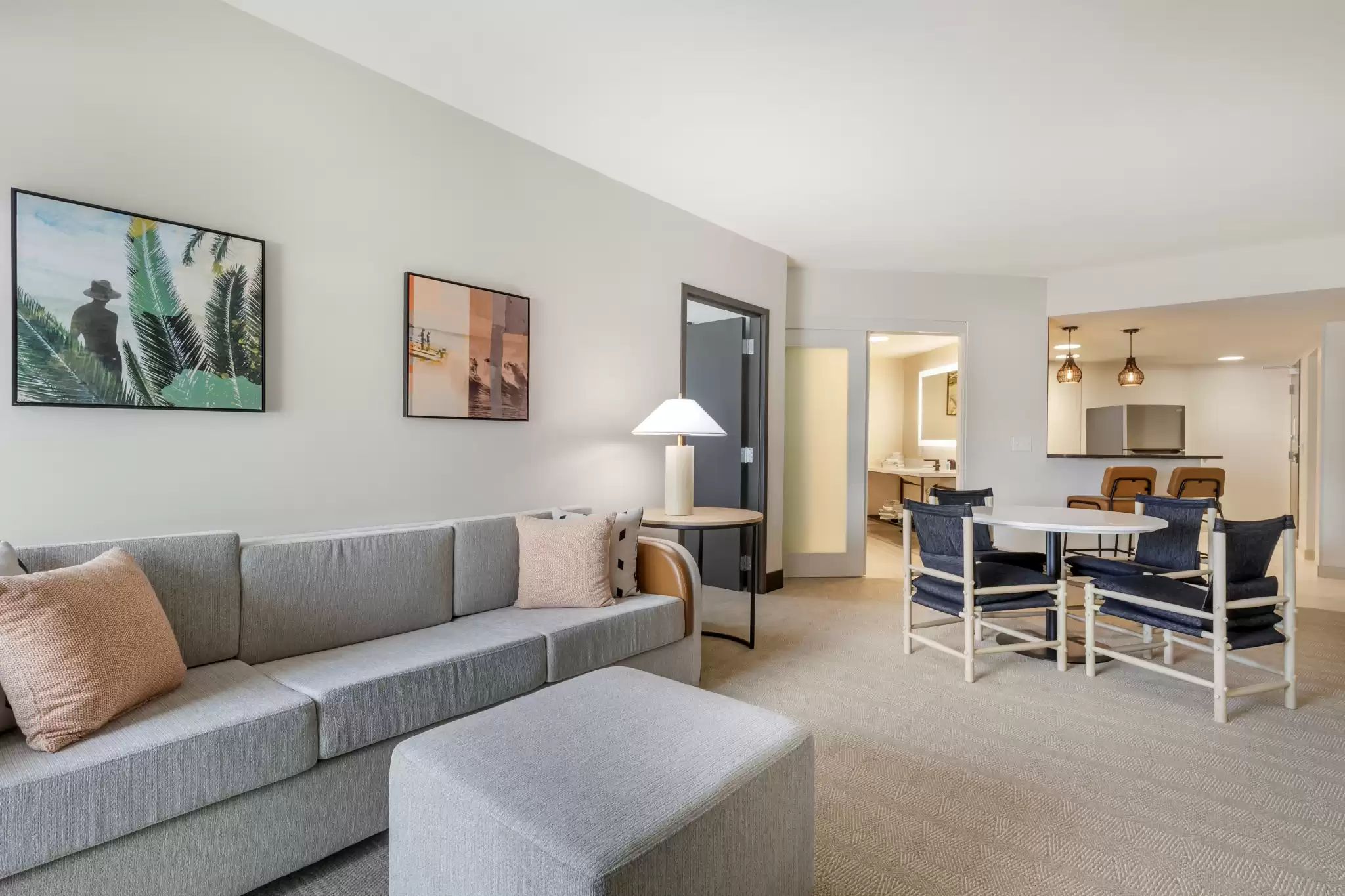 A modern living room with a grey sofa, a small round table, and a dining area with blue chairs.