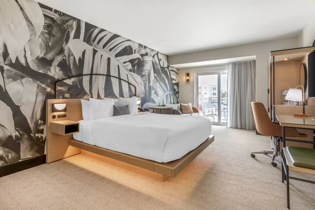 Une chambre d’hôtel moderne, dotée d’un grand lit, d’un bureau et offrant une vue sur la ville.