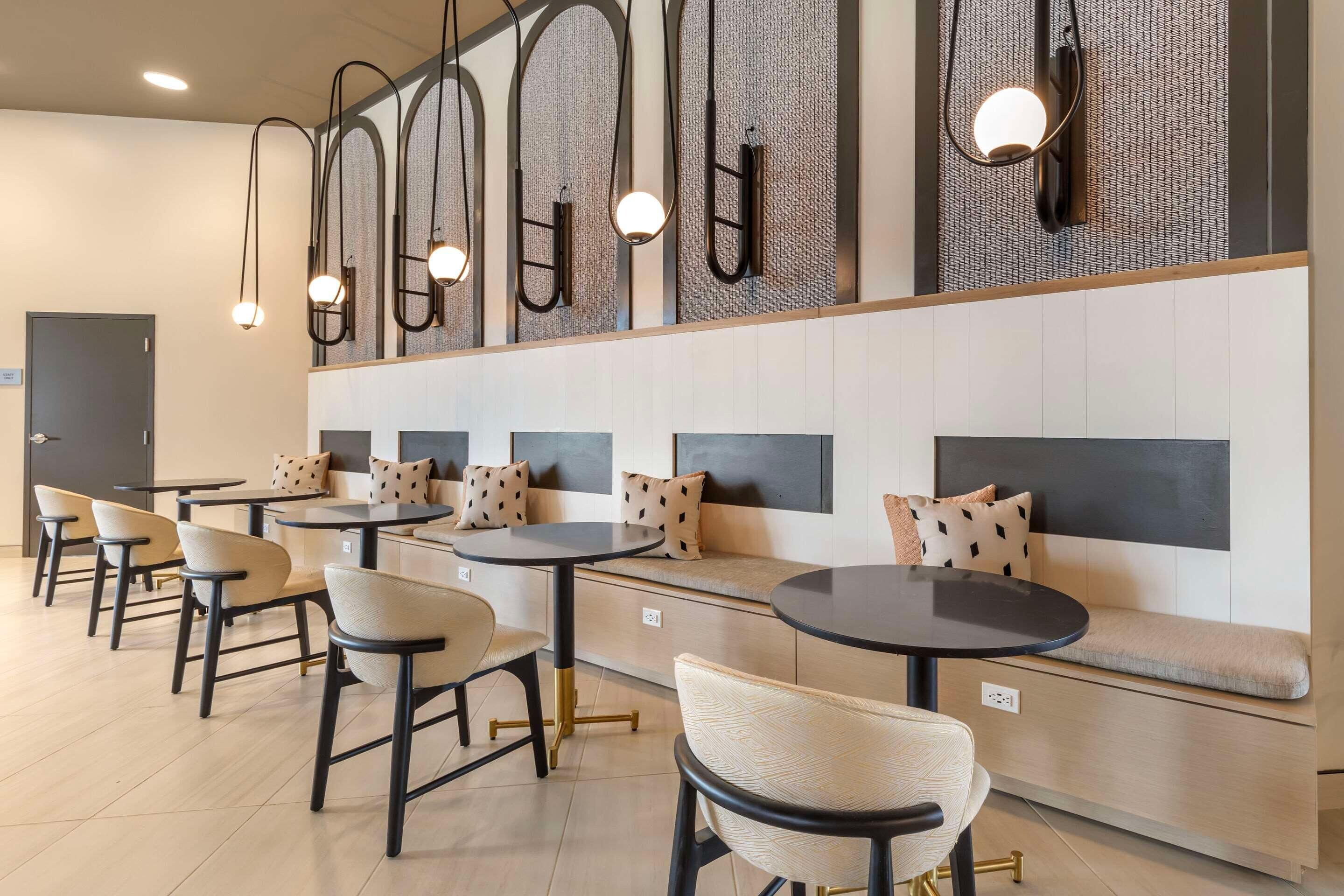 A modern lounge area with round tables and cushioned seating, featuring a unique wall design and pendant lighting.