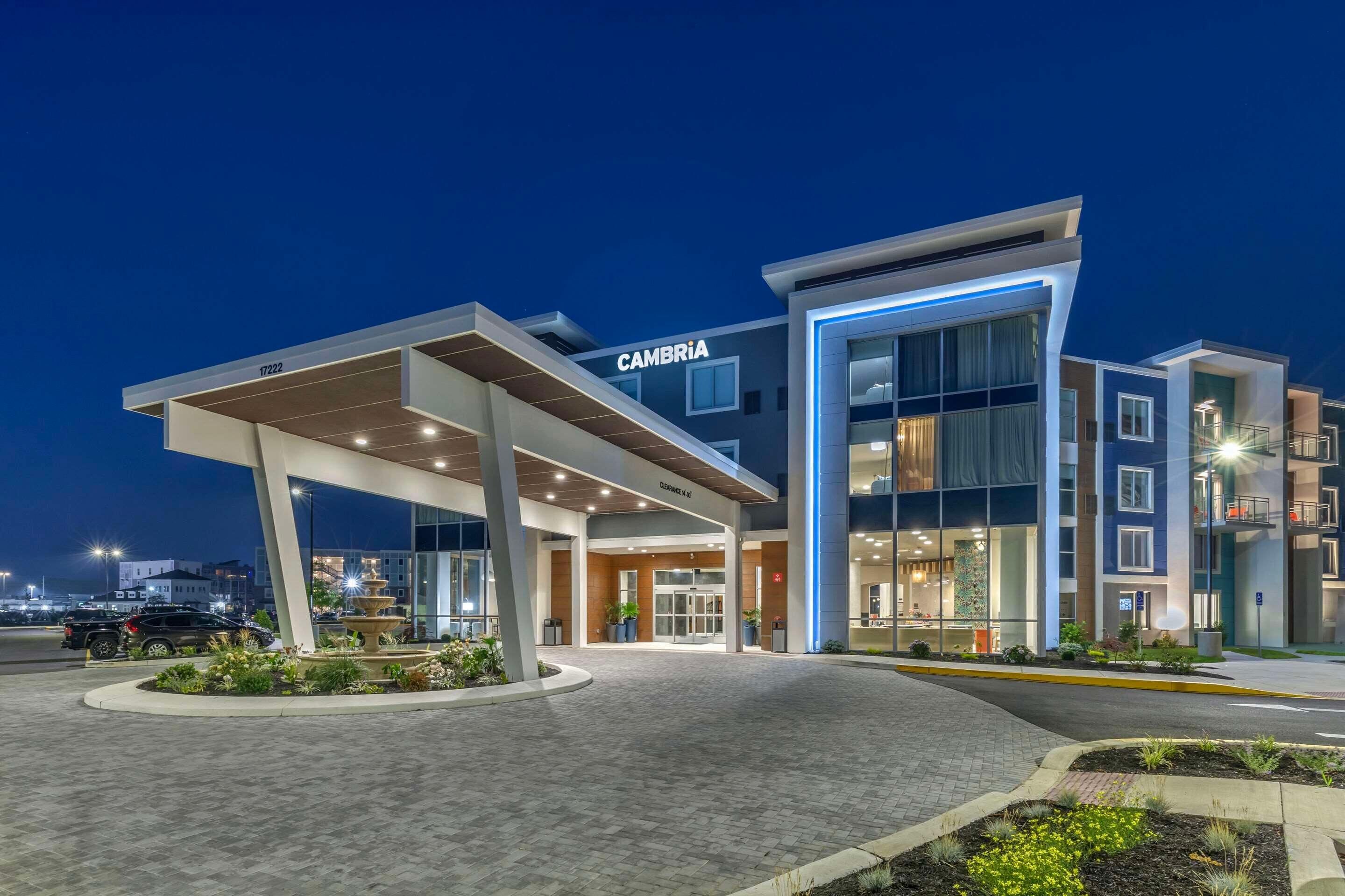 A modern hotel with a prominent "CAMBRIA" sign, a covered entrance, and a well-lit facade.
