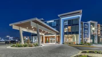 A modern hotel with a prominent "CAMBRIA" sign, a covered entrance, and a well-lit facade.