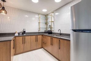 Eine moderne Küche mit Holzschränken, einem Edelstahlkühlschrank, einer Glastrennwand und einer schwarzen Arbeitsplatte.