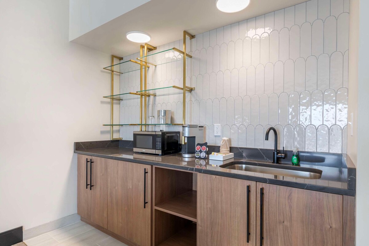 Μια σύγχρονη κουζίνα με εντοιχισμένο φούρνο μικροκυμάτων, καφετιέρα και νεροχύτη από ανοξείδωτο ατσάλι.