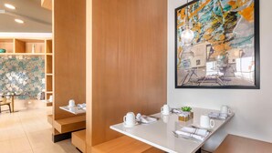 Ein moderner Essbereich mit Holzbänken und -tischen, weißem Geschirr und einem farbenfrohen, abstrakten Gemälde an der Wand.