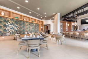 A modern dining area with round tables and cushioned chairs, a decorative wall with a leaf pattern, and a bar area with a staircase. - Cambria Hotel Rehoboth Beach (Rehoboth Beach)