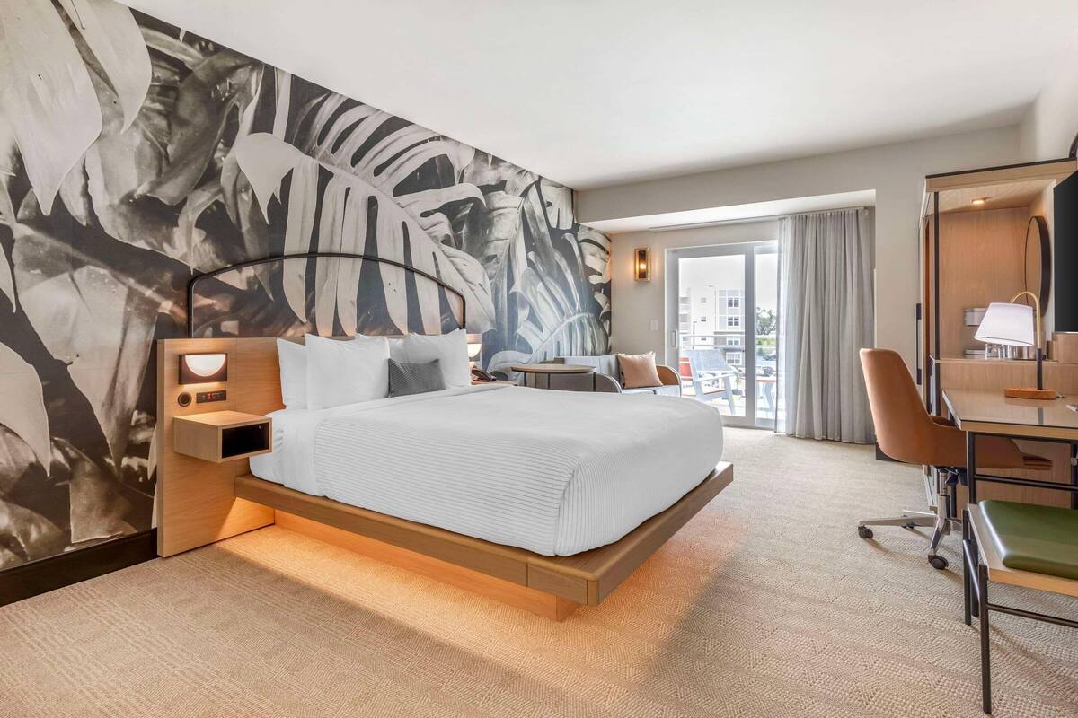 A hotel room with a large bed, a desk, a chair, and a view of the city through the window.