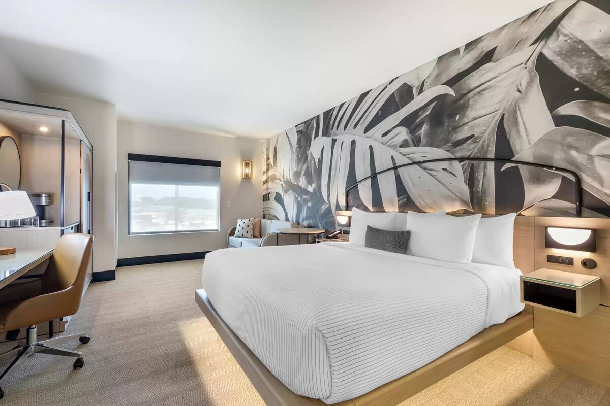 A modern hotel room with a large bed, a desk, and a view of the city.