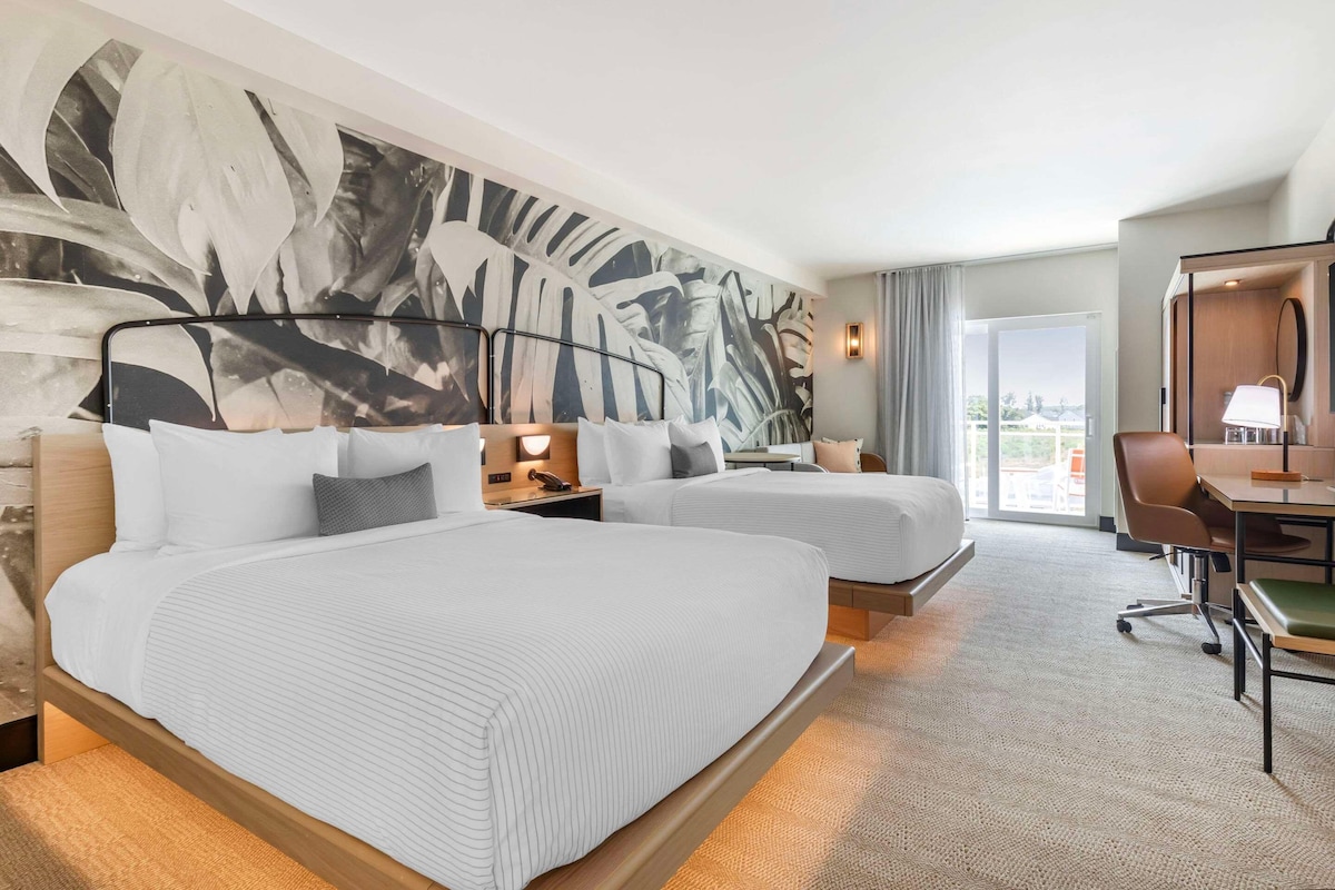 A hotel room with two beds, a desk, a chair, and a large window.