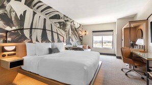 Ein Hotelzimmer mit einem großen Bett, einem Schreibtisch, einem Sessel, einem Nachttisch und einer Wandleuchte.