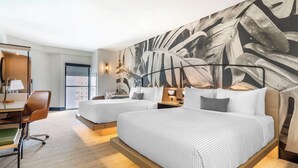 Ein Hotelzimmer mit zwei Betten, einem Schreibtisch mit Stuhl und einer großen Wand mit Blattmuster.