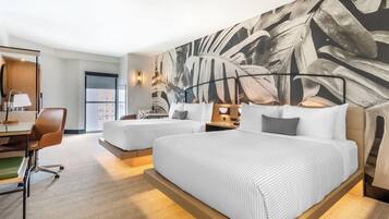 Une chambre d’hôtel avec deux lits, un bureau avec une chaise et un grand mur décoré d’un motif de feuilles.