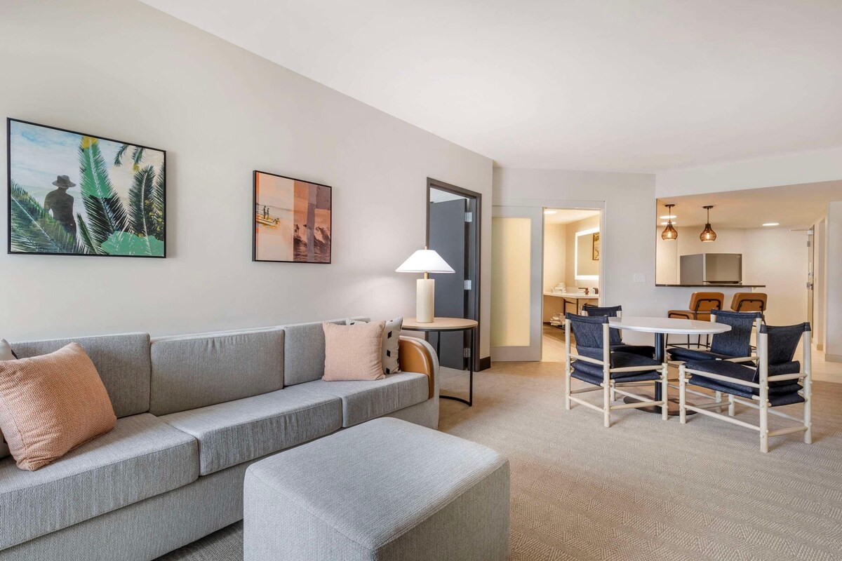 A modern living room with a grey sofa, a small round table, and a dining area with blue chairs.