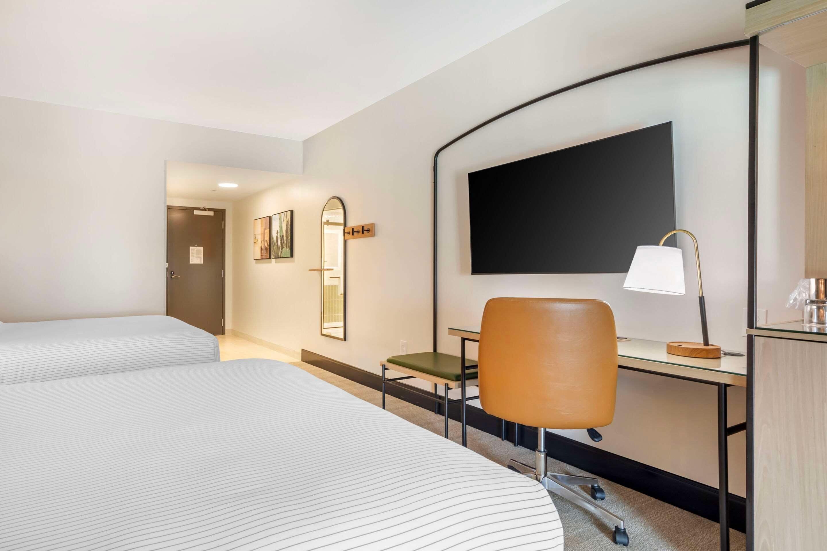 A hotel room with two beds, a desk, a chair, a TV, and a mirror.