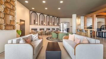 A modern lobby with sofas, a coffee table, and a dining area with chairs and tables.