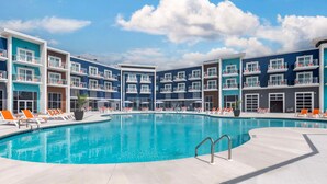 Ein modernes Hotel mit einem zentral gelegenen Schwimmbecken, umgeben von orangefarbenen Liegestühlen und blauem Himmel.