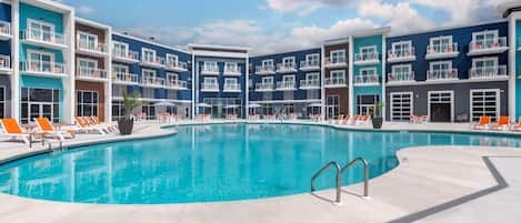 A modern hotel with a central swimming pool surrounded by orange lounge chairs and a clear blue sky.