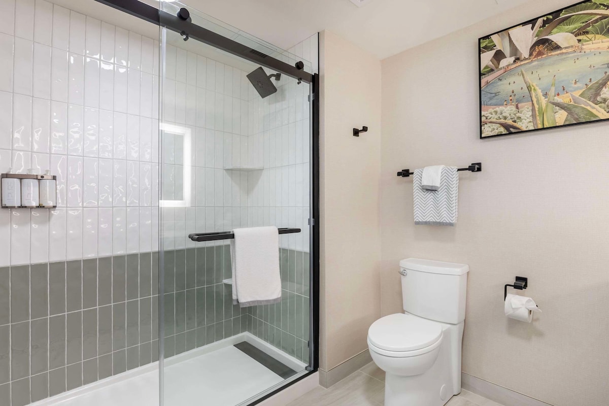 Une salle de bain moderne dotée d’une douche à parois de verre, de toilettes et d’un porte-serviettes fixé au mur.
