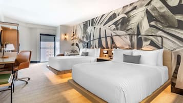 A hotel room with two beds, a desk, a chair, and a large leaf-patterned wall.