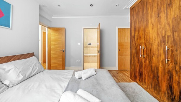 Una camera d'albergo con un letto grande, un armadio in legno e un bagno visibile attraverso una porta aperta.