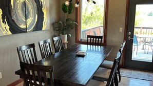 Een eetkamer met een donker houten tafel en stoelen, een moderne lamp en een groot abstract schilderij aan de muur.