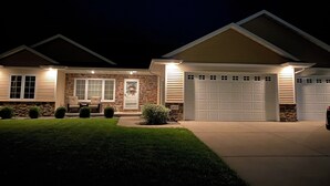 A two-story house with a stone facade, a front porch with seating, and a garage. - Entertainer's Dream - Quick drive to Lambeau - Hot Tub, Bar, & 85" TV. (Green Bay)
