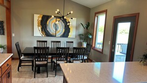 A modern kitchen with a dining area, featuring a large abstract painting, a chandelier, and a view through a window. - Entertainer's Dream - Quick drive to Lambeau - Hot Tub, Bar, & 85" TV. (Green Bay)