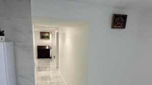 A hallway with white walls and a marble floor leading to a dark-toned room. - Appartement Calme Moderne Proche de Disneyland Wifi & Café Gratuit (Bussy-Saint-Georges)