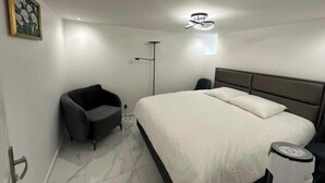 A modern hotel room with a bed, a chair, a floor lamp, and a painting on the wall. - Appartement Calme Moderne Proche de Disneyland Wifi & Café Gratuit (Bussy-Saint-Georges)