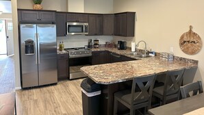 Een moderne keuken met donkere kasten, roestvrijstalen apparatuur, granieten werkbladen en een centraal eiland met barstoelen.