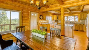 A wooden cabin interior with a dining table, chairs, a chandelier, and a kitchen area. - Scenic 4BR Log Cabin w/ MTN views (Pagosa Springs)