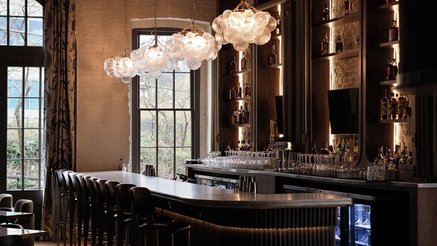 A bar area with a counter, stools, and a hanging light fixture. - The Delegate (Frankfort)