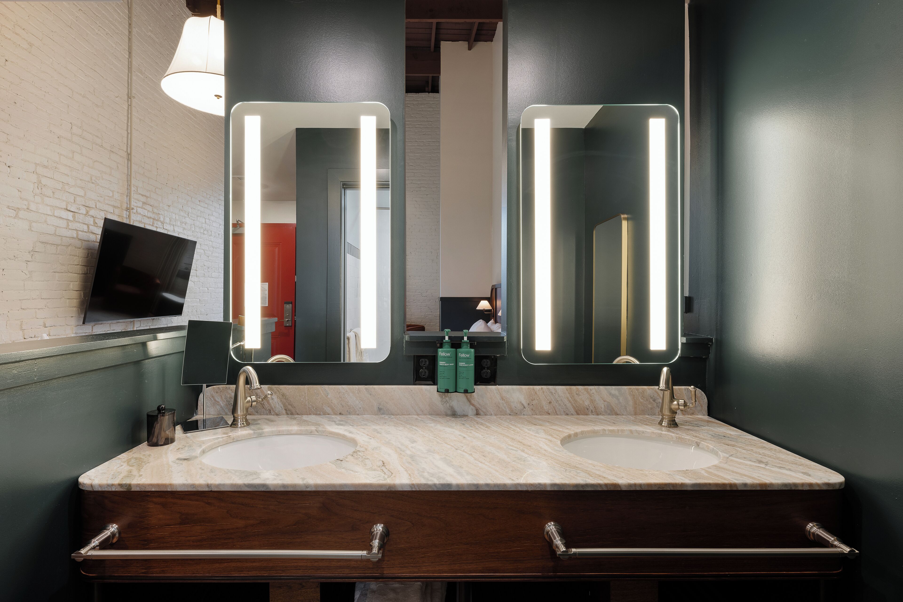 A bathroom with two sinks, a mirror, and a television on the wall.