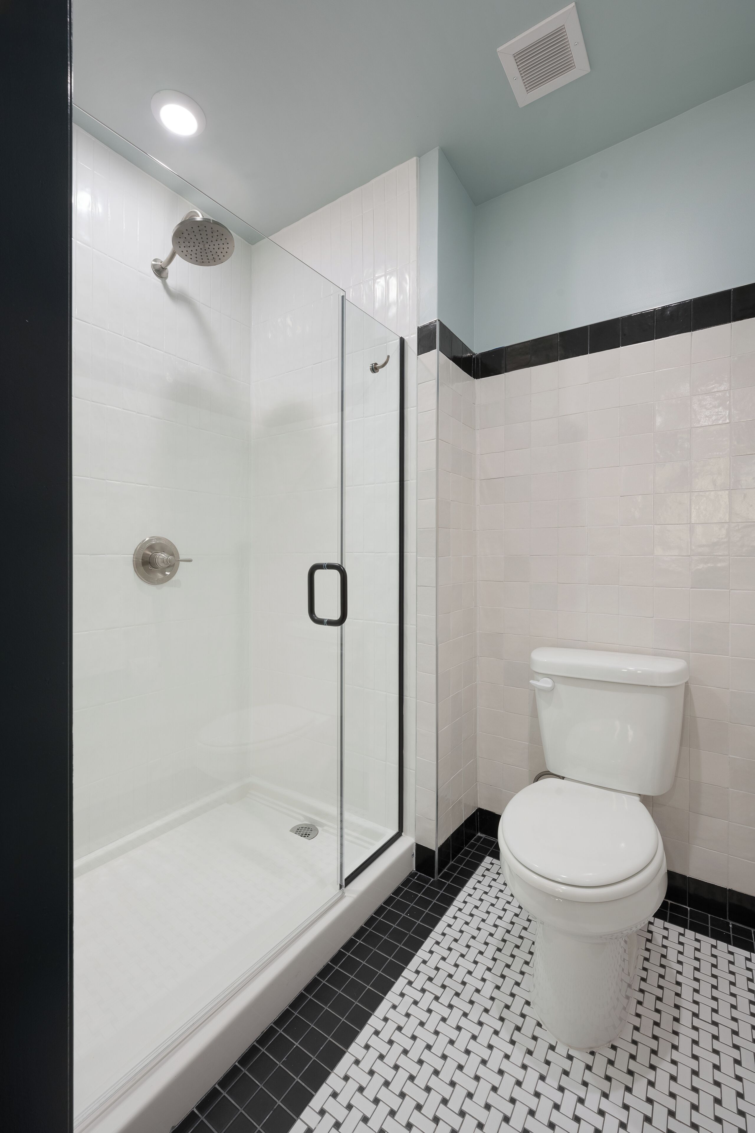 A modern bathroom with a glass-enclosed shower, a white toilet, and a black and white tiled floor.