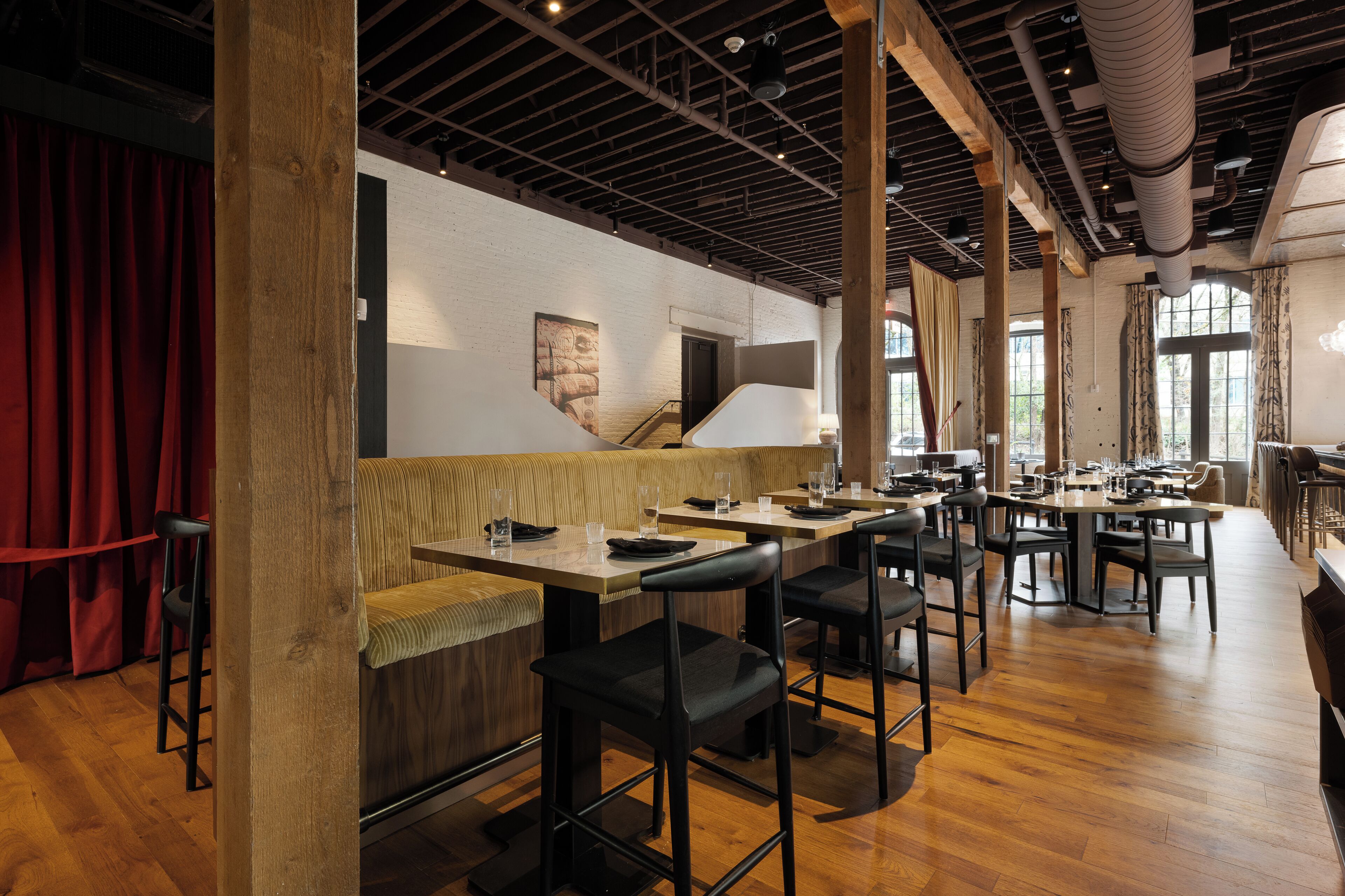 A restaurant with wooden floors, high ceilings, and exposed beams. There are multiple tables and chairs arranged for dining.
