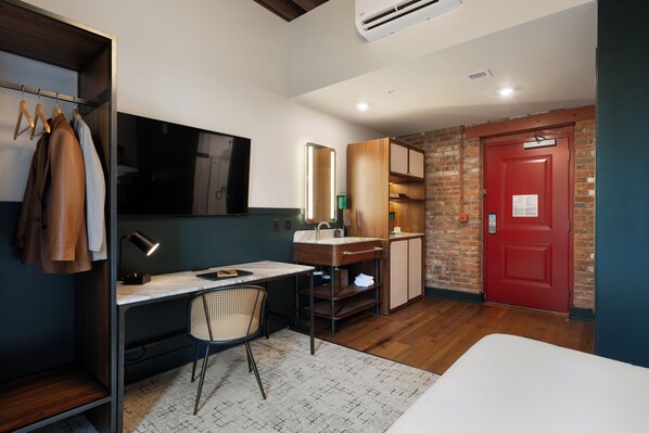A compact hotel room with a desk, chair, and a bed. - The Delegate (Frankfort)