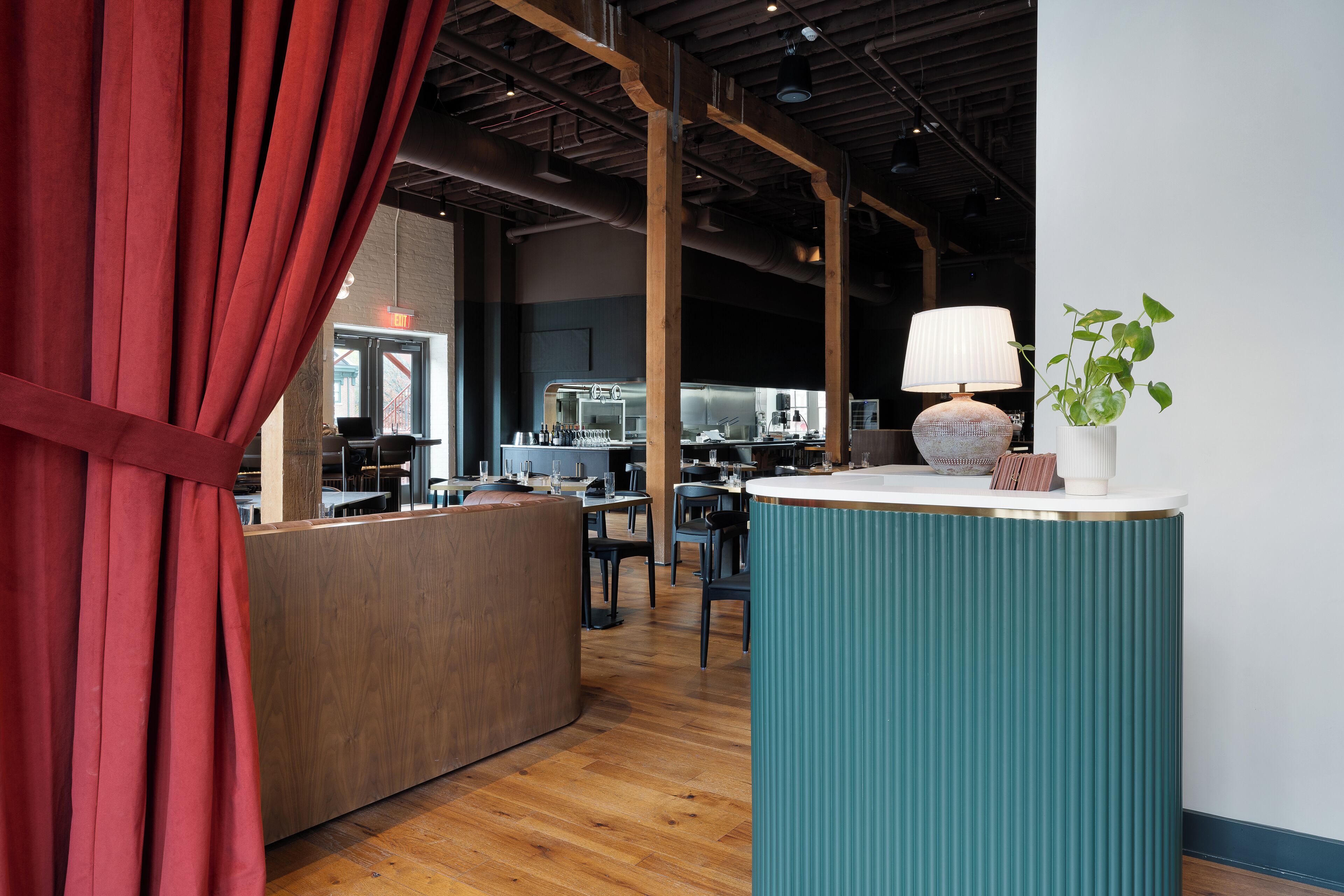 A modern interior with a wooden reception desk, a teal accent wall, and a large window with red curtains.