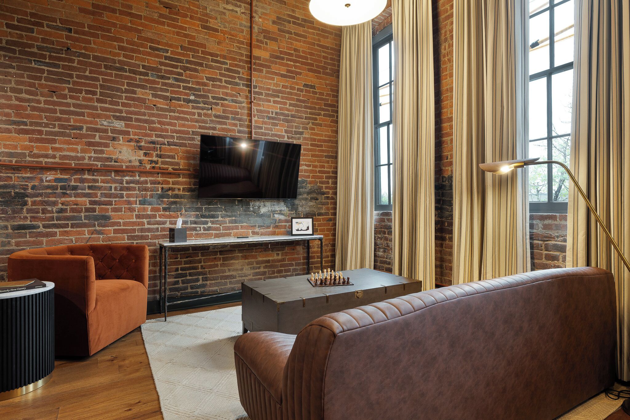A modern living room with a brick wall, a flat-screen TV mounted above a wooden coffee table, and a leather sofa.
